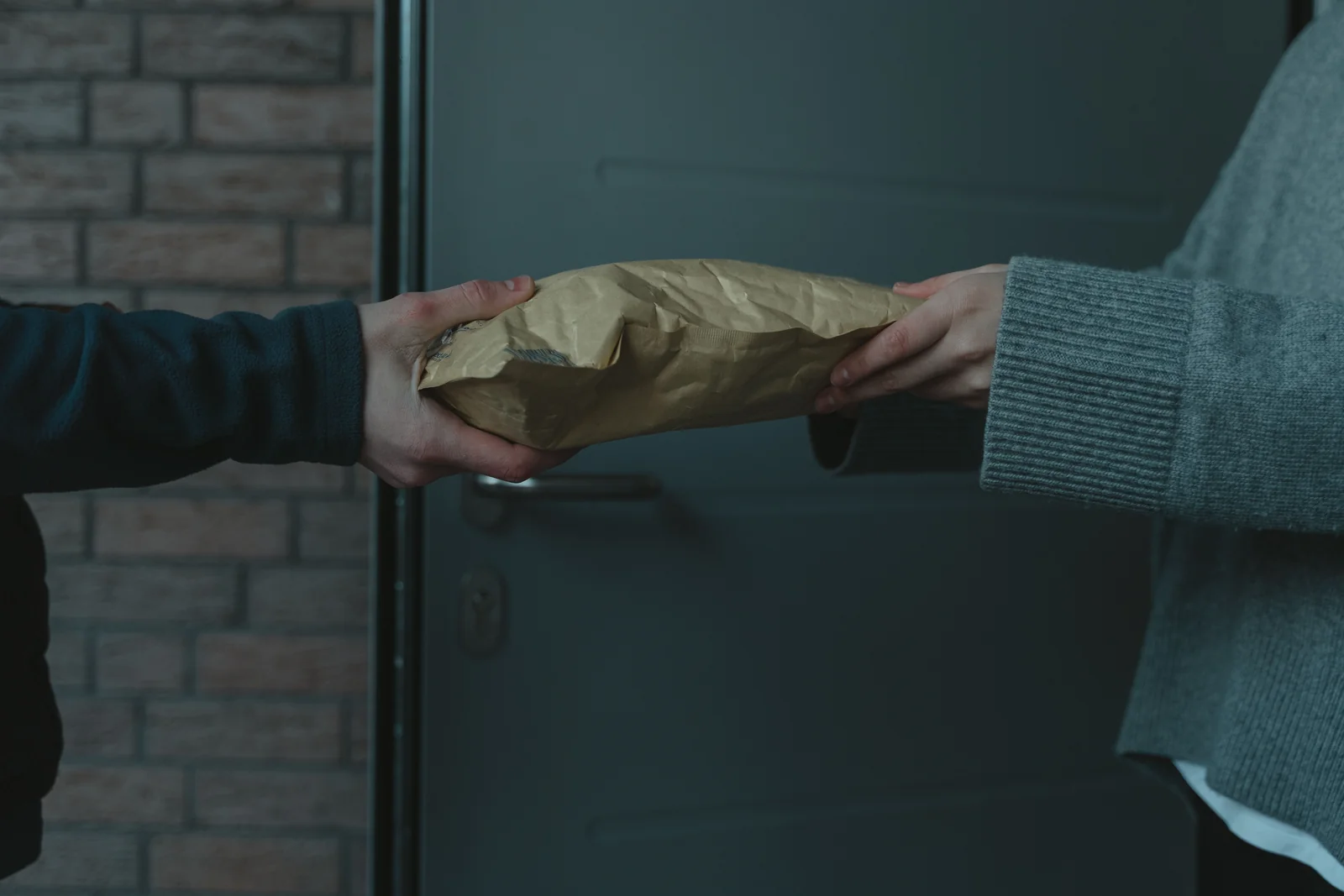 Hands passing a securely packed parcel at a doorway.