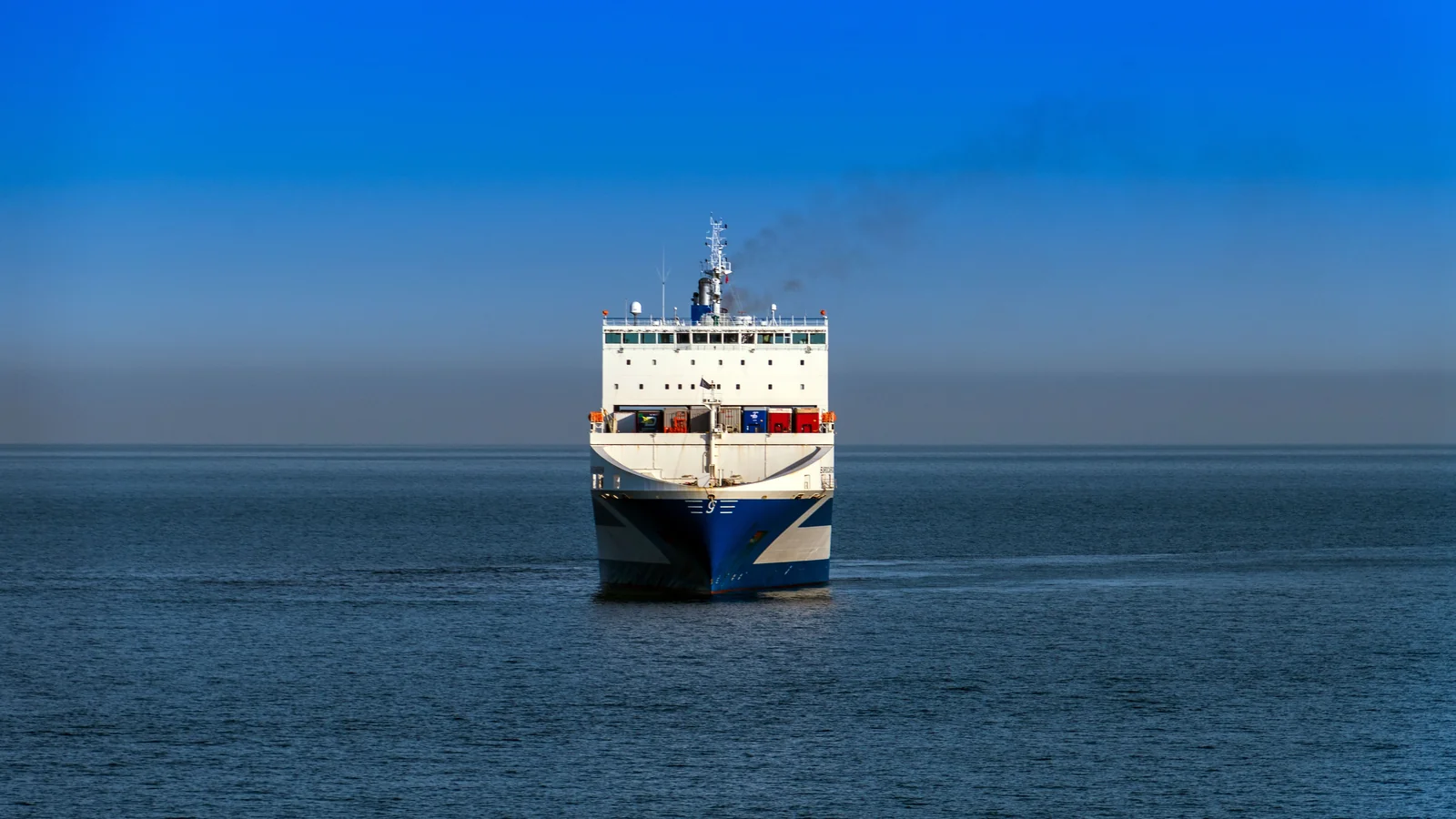 A cargo vessel approaching across calm blue water.