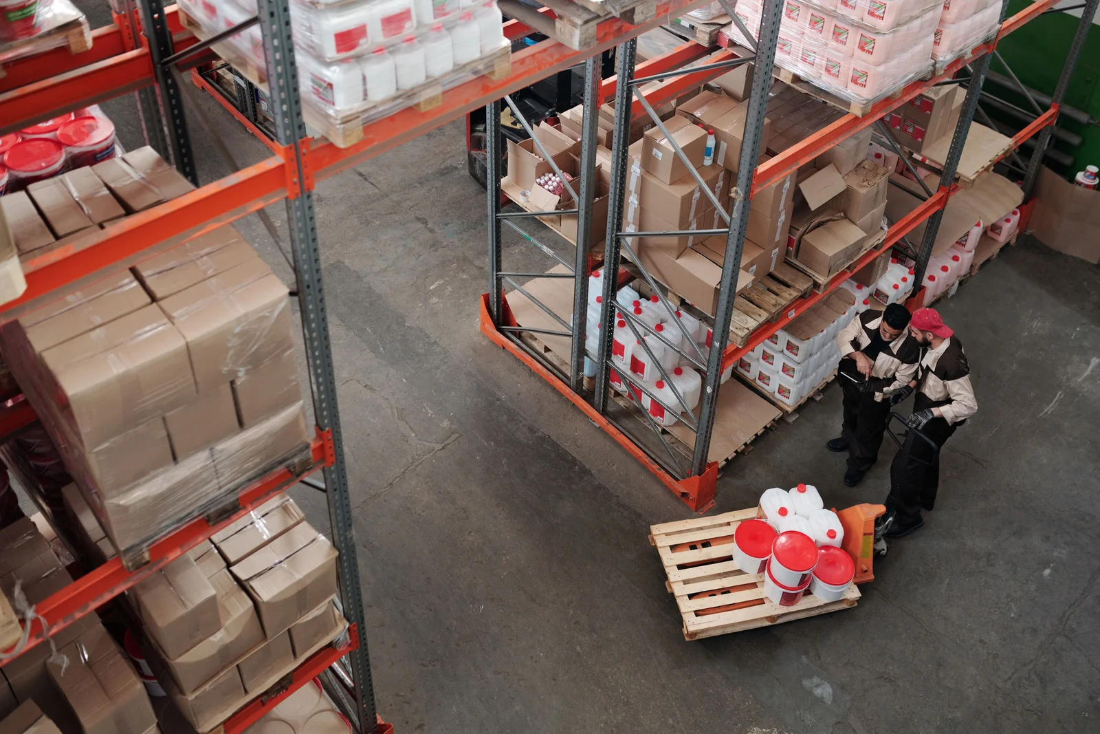 Warehouse staff checking stored goods and inventory among pallet shelves.