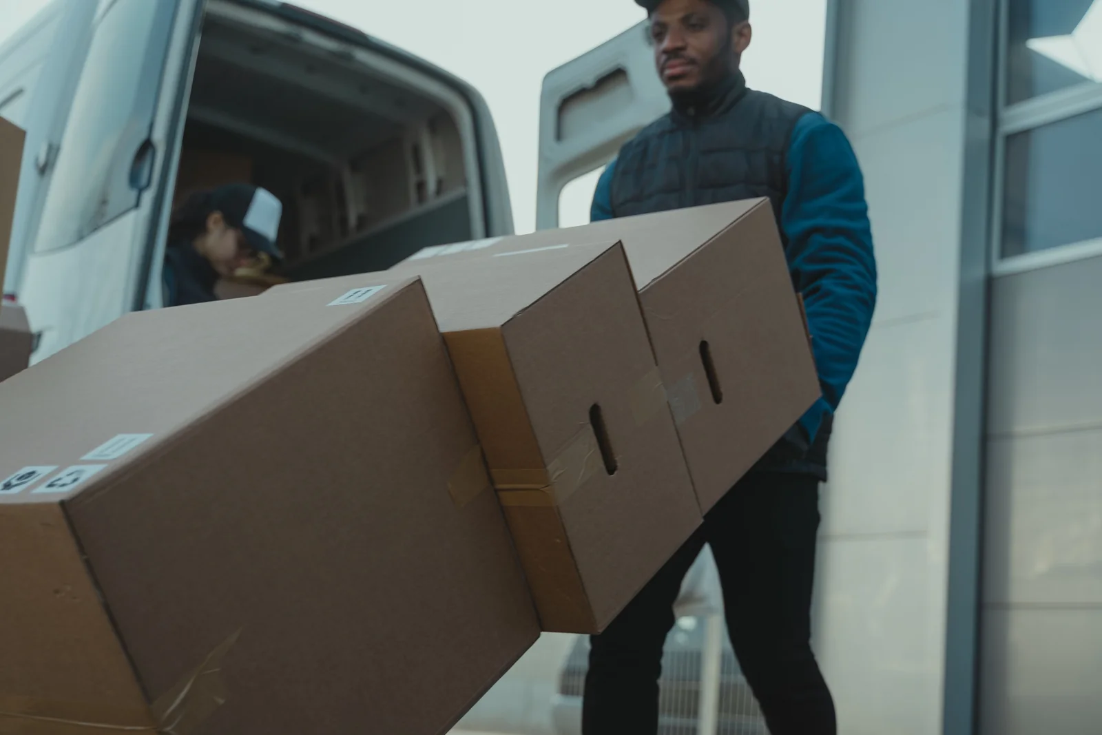 A courier with packaged goods beside an open delivery van.