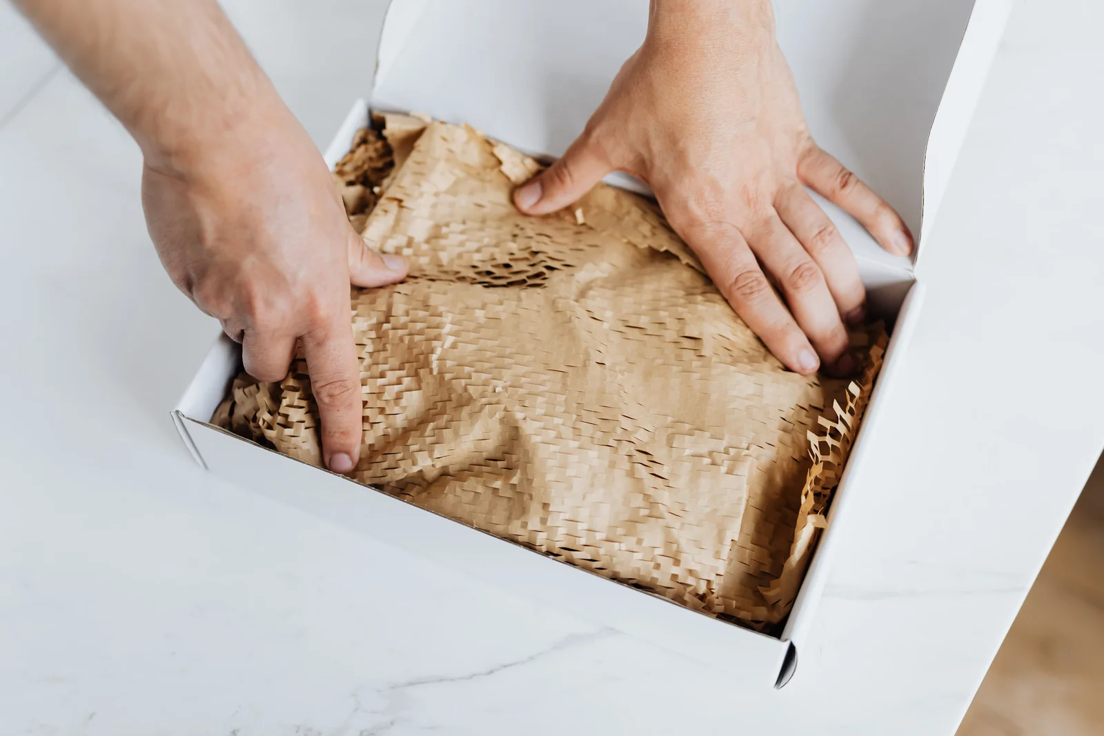 Hands placing protective paper around an item in a shipping box.